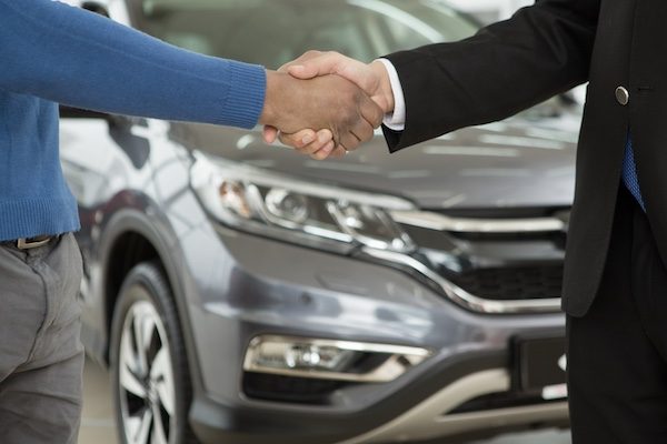 Cropped close up of a salesman shaking hands with his male African client after selling a new car buying buyer consumerism customer client service deal agreement contract partnership sales discount