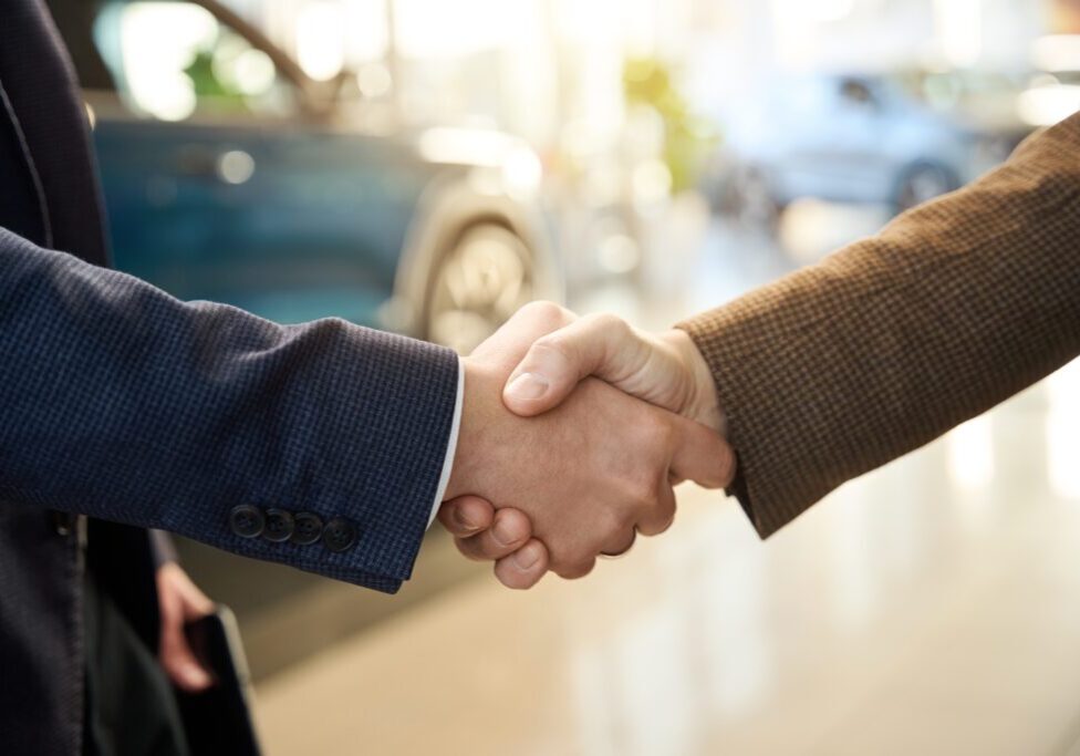 Two people shaking hands in a car dealership